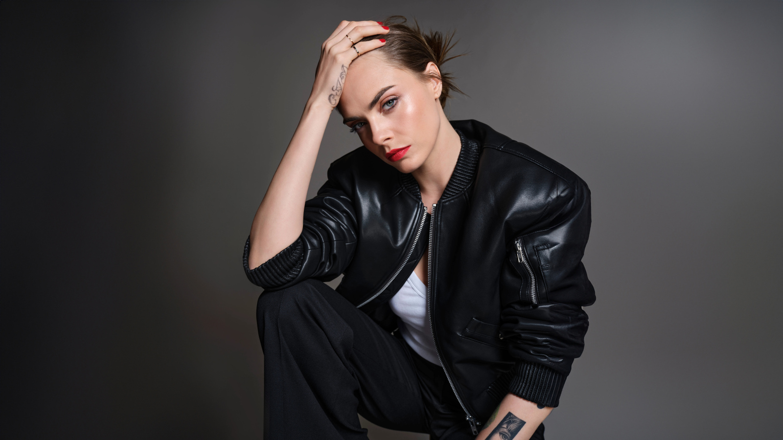 Актриса Кара Делевинь в черной кожаной куртке на сером фоне