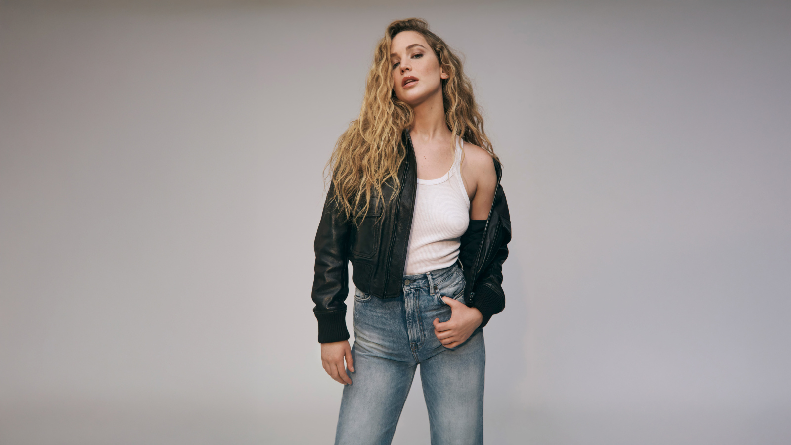 Американская актриса Дженнифер Лоуренс  в джинсах на сером фоне