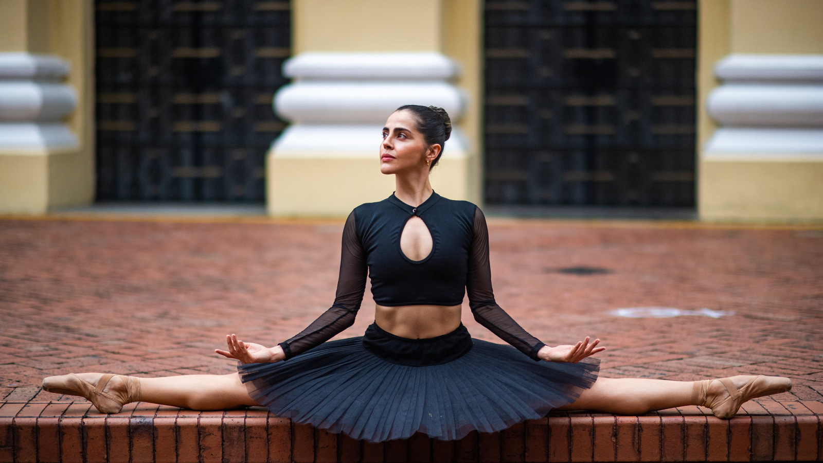 Девушка балерина в черном сидит на шпагате