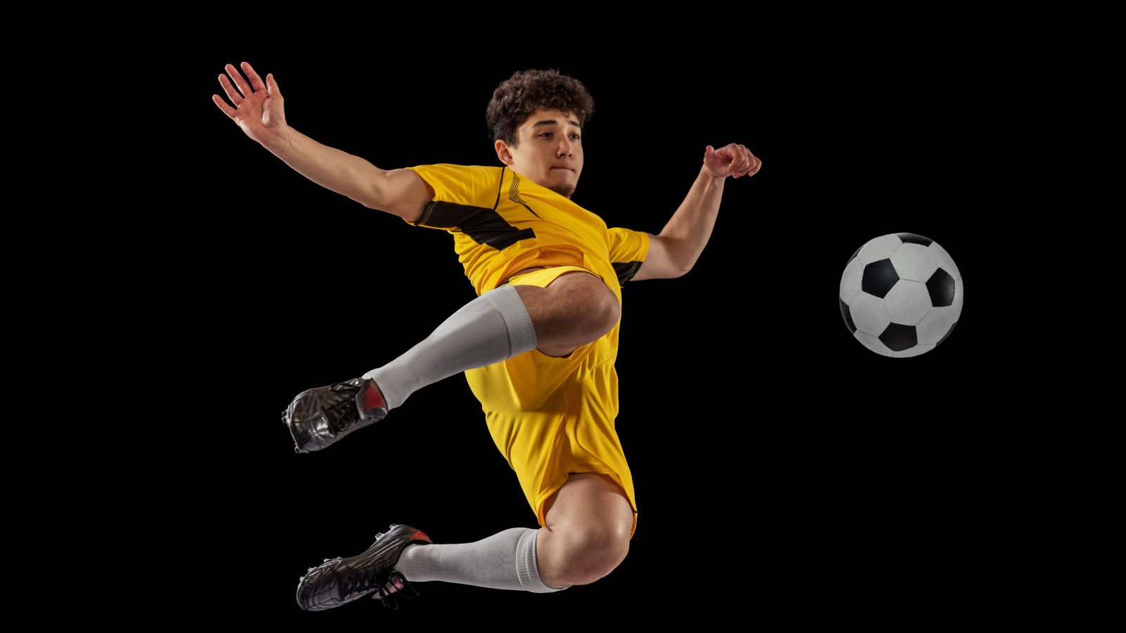 Мужчина футболист отбивает мяч на черном фоне