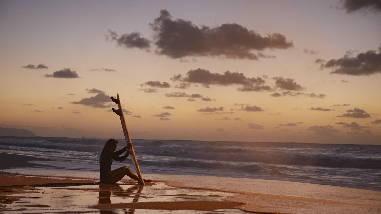 Девушка серфингистка сидит на берегу моря