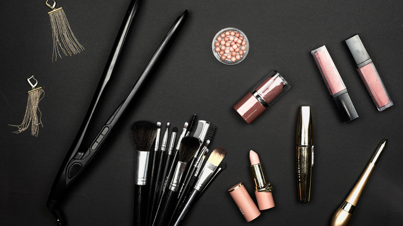 Кисточки с косметикой и плойкой на черном фоне