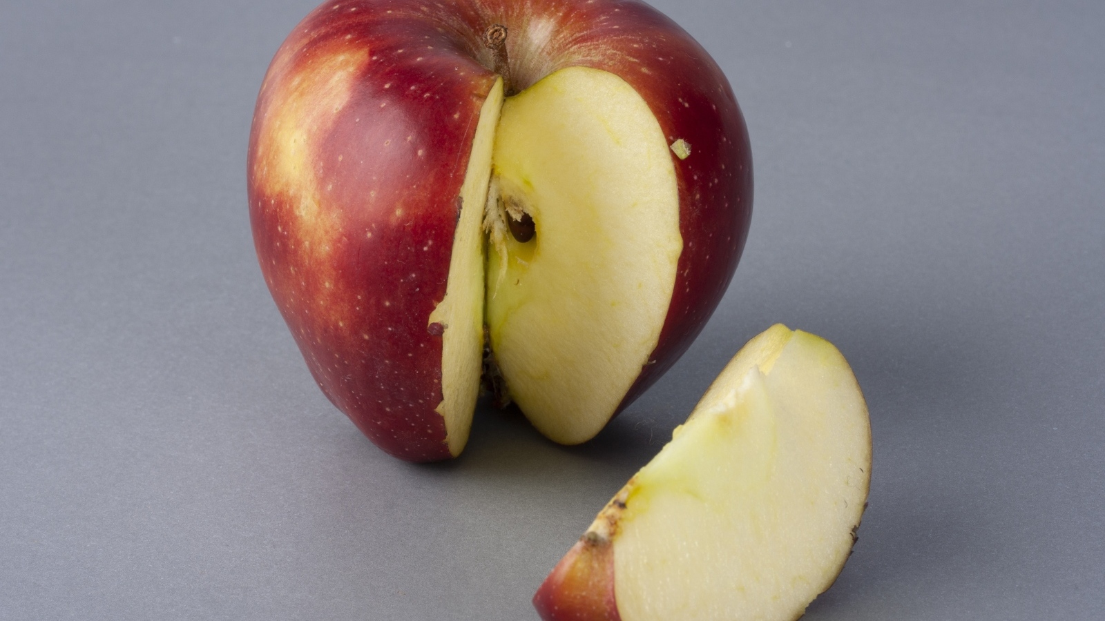 Разрезанное красное яблоко на сером фоне