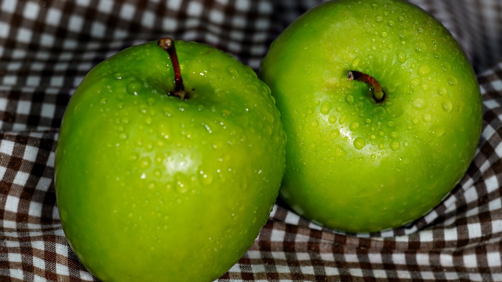 Два мокрых зеленых яблока на скатерти