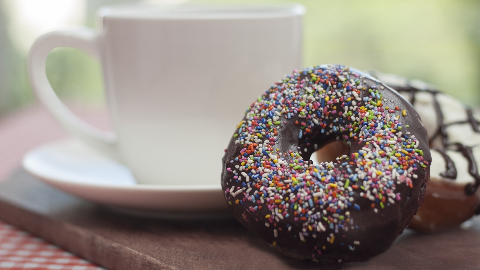 Донат с шоколадной глазурью и сладкой посыпкой на столе с чашкой чая