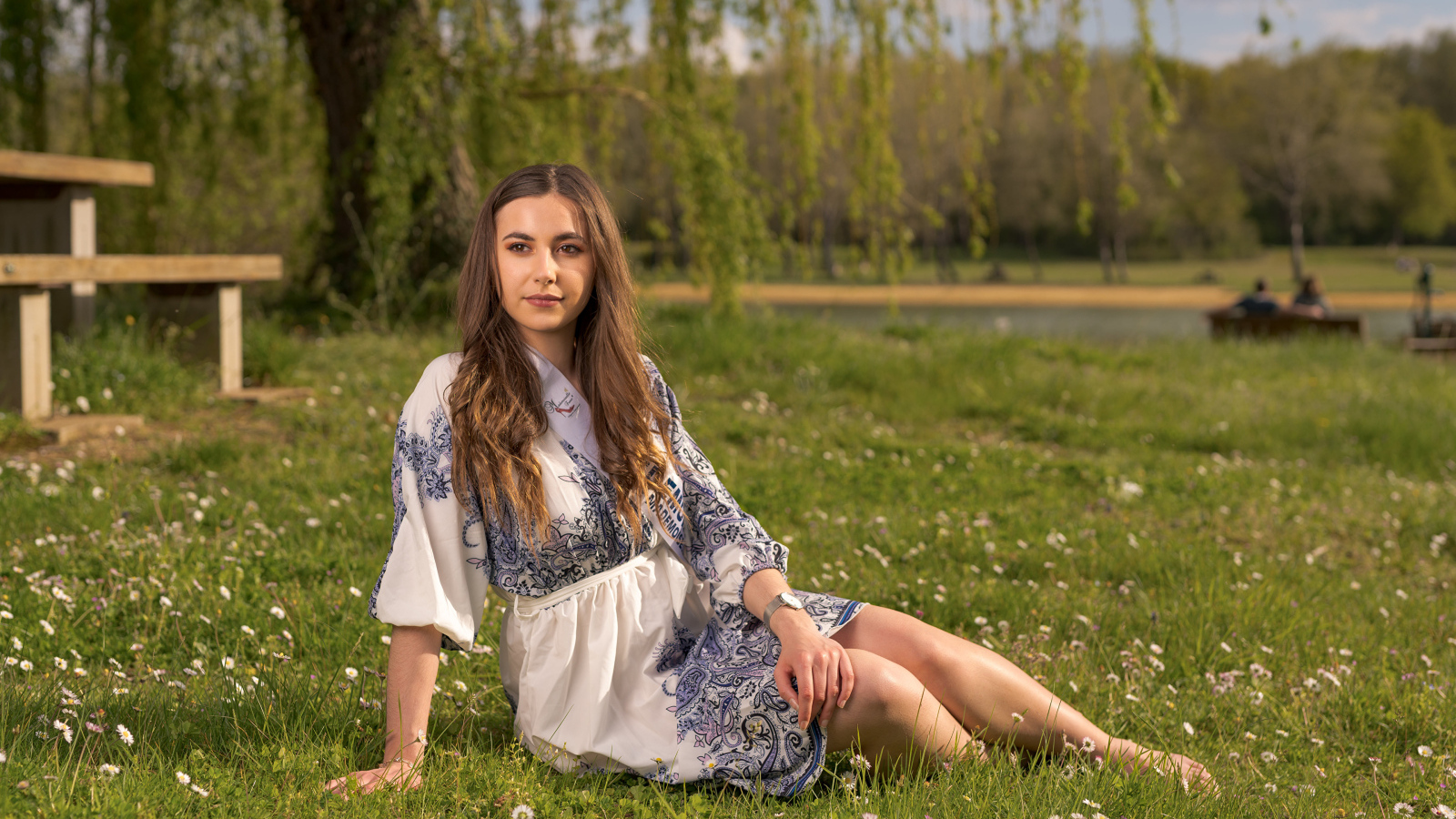 Красивая девушка в платье сидит на зеленой траве в парке