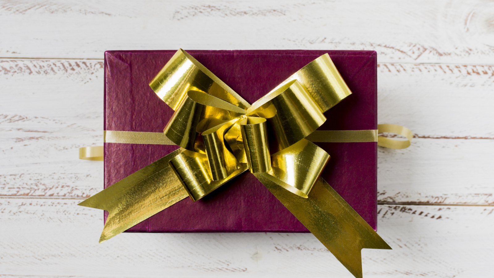 Красная коробка с подарком с золотым бантом на столе