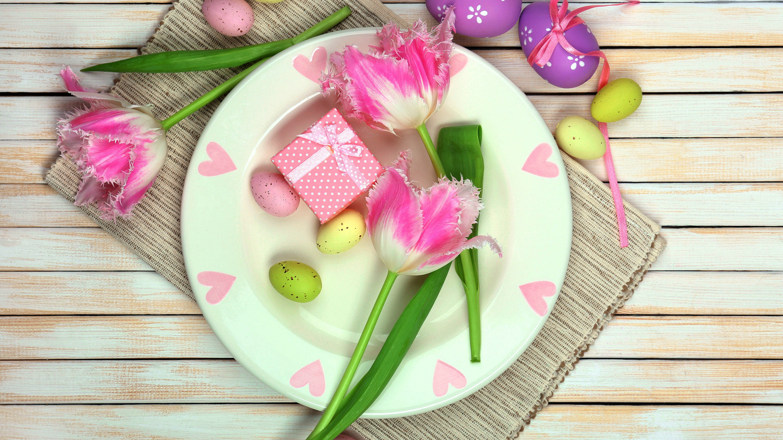 Пасхальные яйца с тюльпанами на тарелке на столе