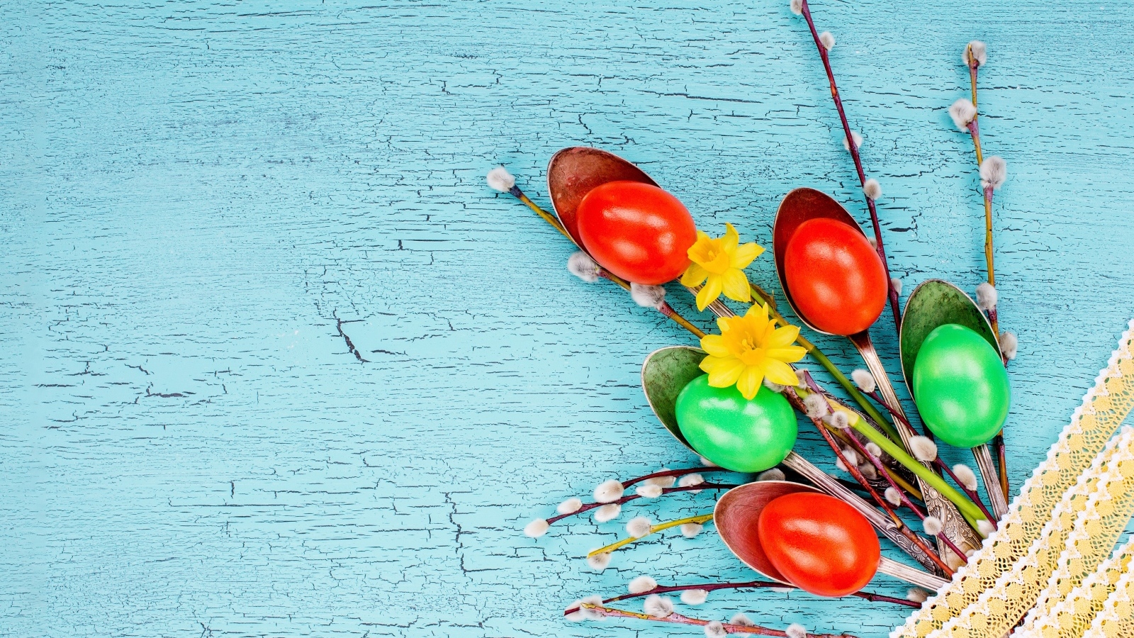 Ложки с разноцветными яйцами и ветками вербы на голубом фоне на Пасху