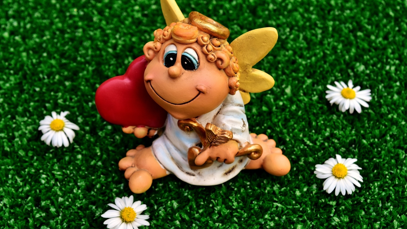 Статуэтка ангела на зеленой траве с белыми ромашками