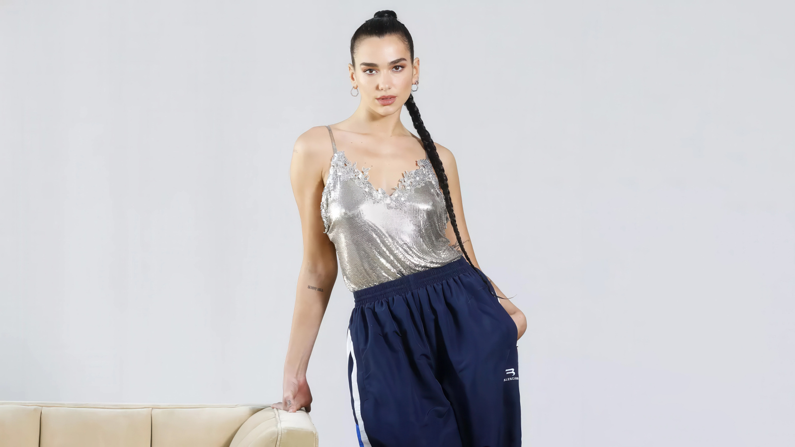 Певица Дуа Липа в спортивных штанах на сером фоне