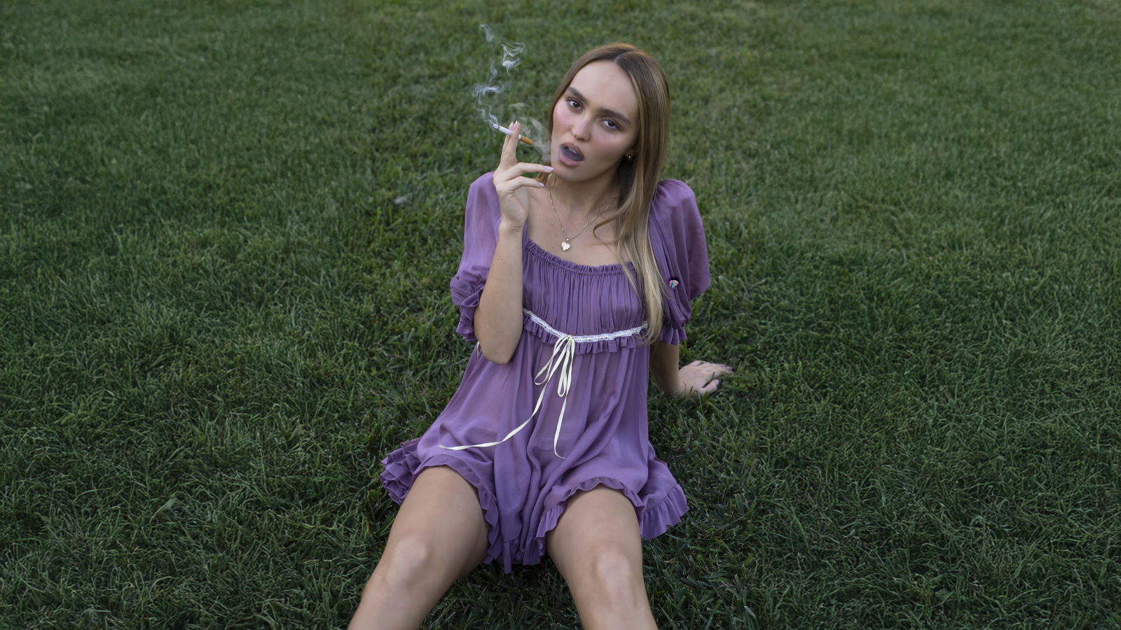 Молодая Лили-Роуз Депп с сигаретой сидит на траве