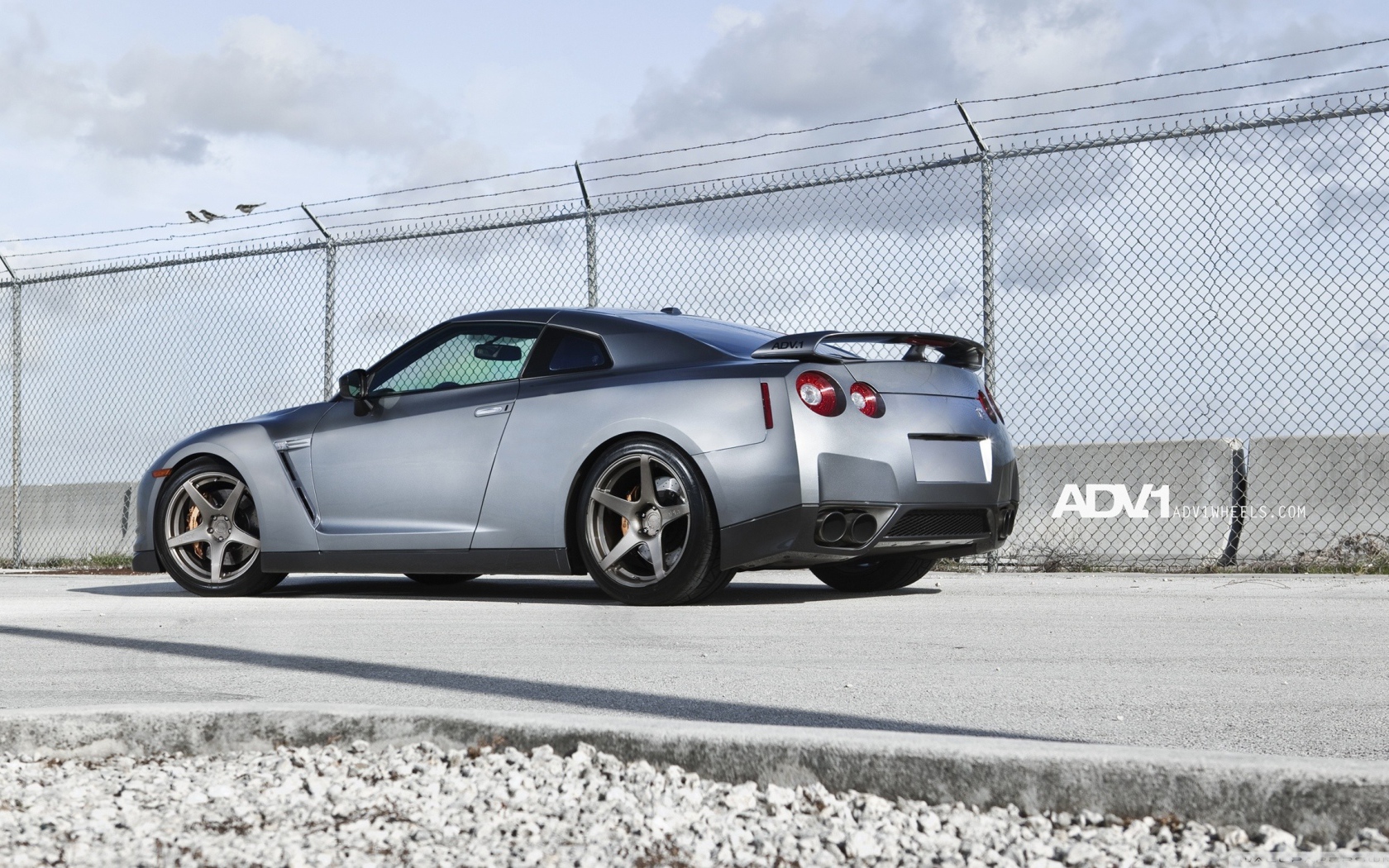 Серый Nissan Skyline GT-R R35 у забора из сетки