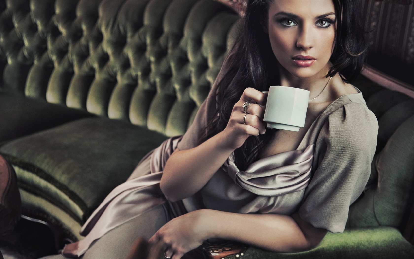 Брюнетка с чашкой кофе сидит на диване