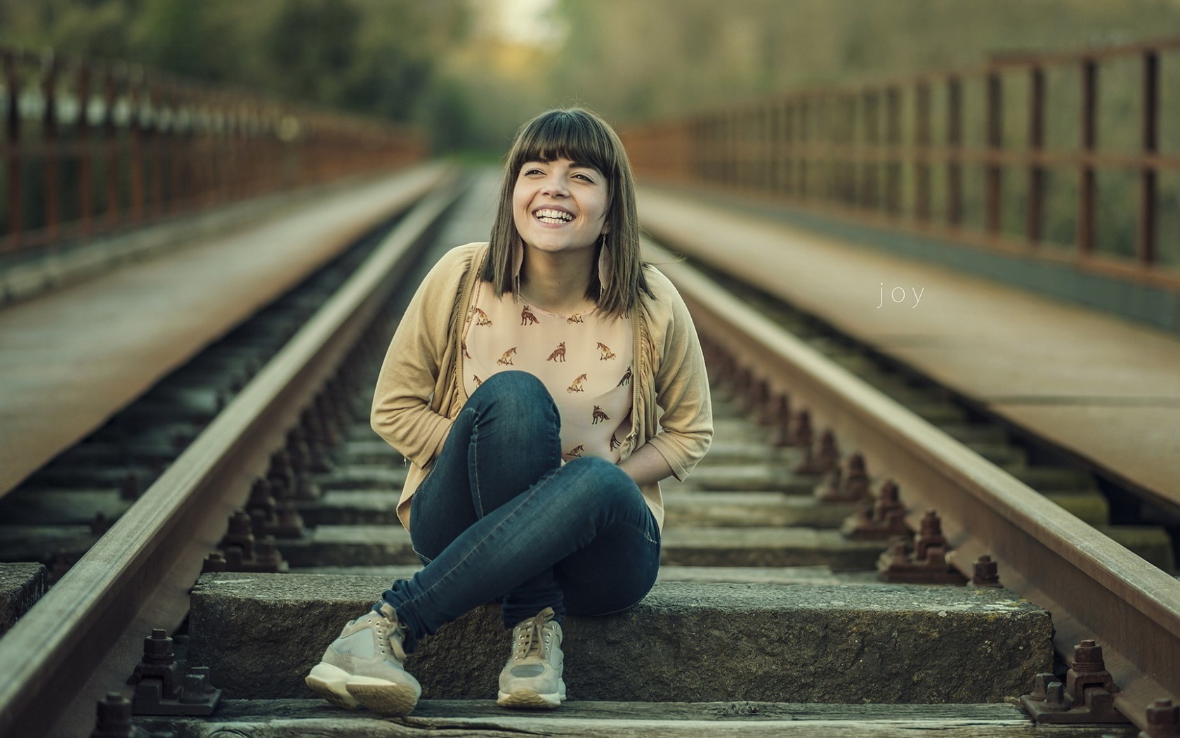 Девушка улыбается сидя на рельсах