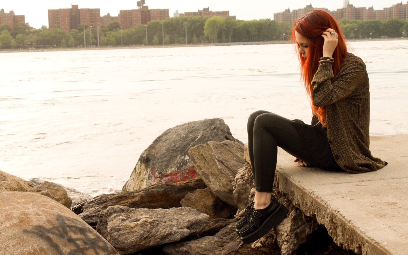 Рыжая девушка сидит на плитах набережной