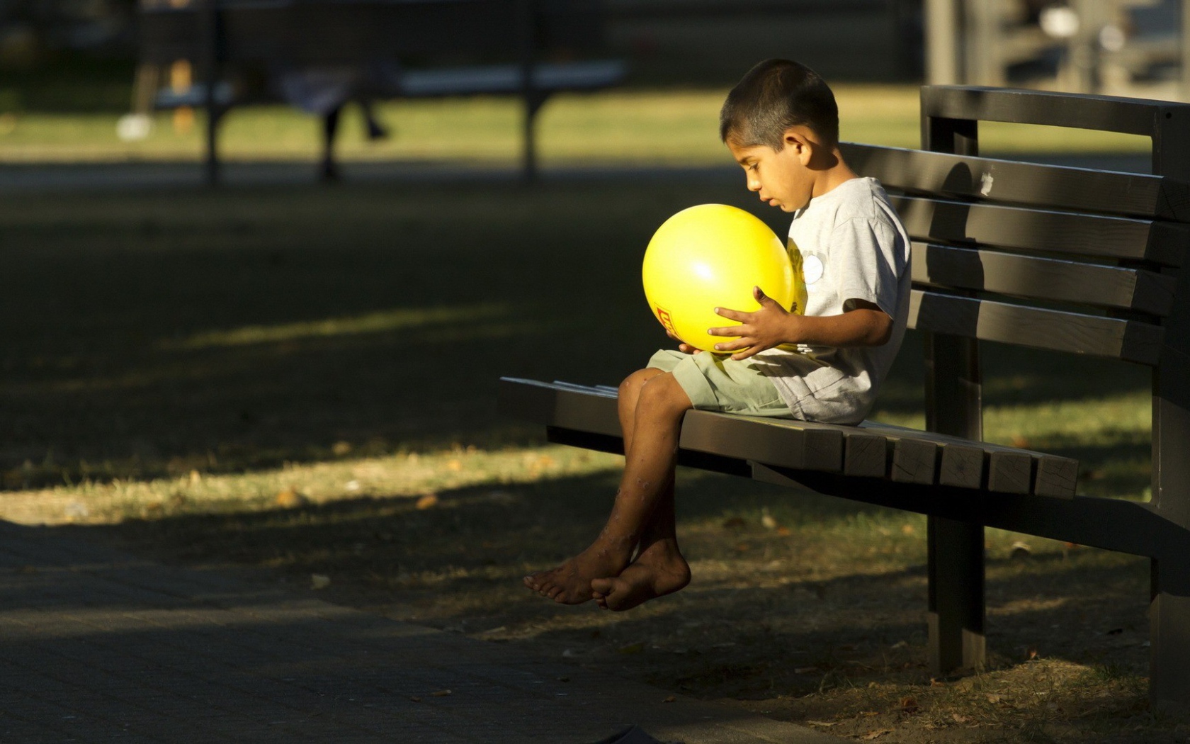 Мальчик сидит на скамье с шариком в руках