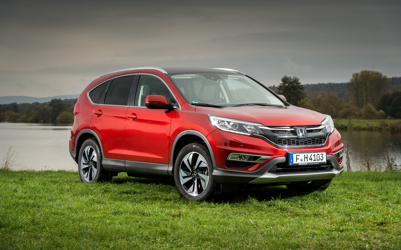 Красный внедорожник Honda CR-V стоит на зеленой траве у реки