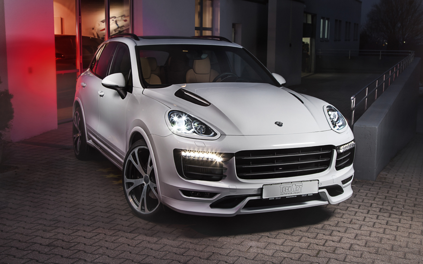 Белый внедорожник Porsche Cayenne с включенными фарами