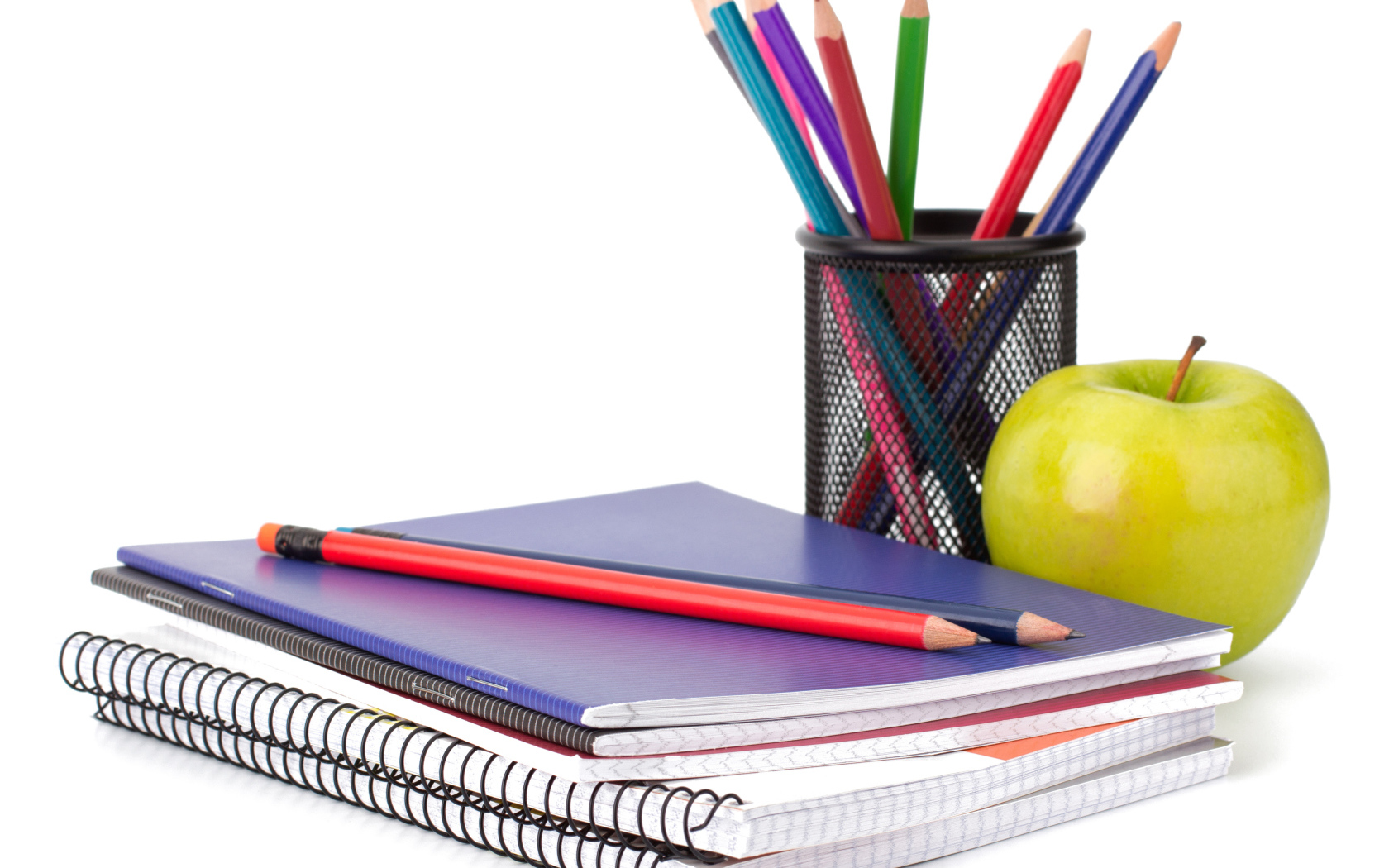 Тетради, карандаши и зеленое яблоко на белом фоне