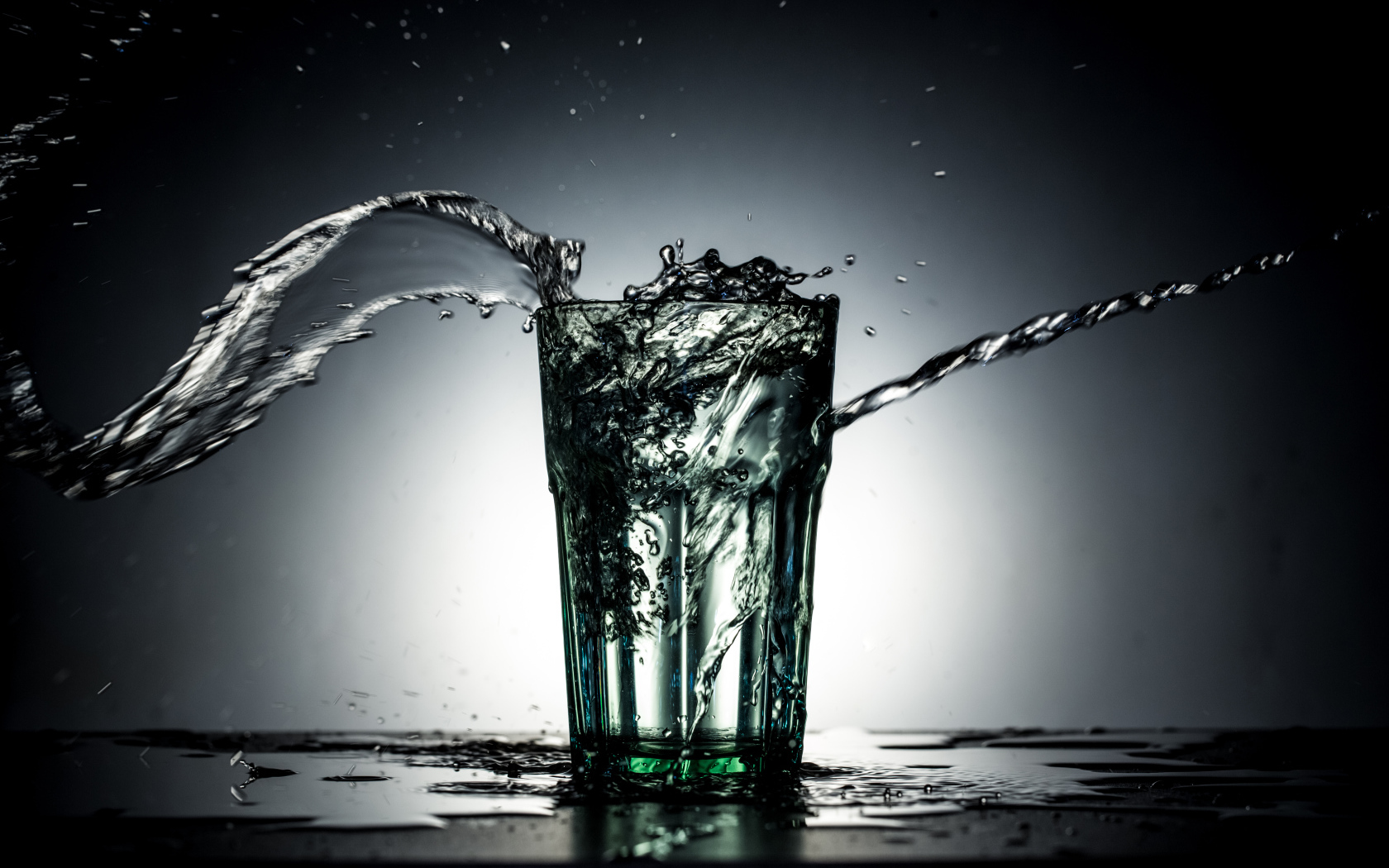 Брызги воды из стакана с водой на сером фоне