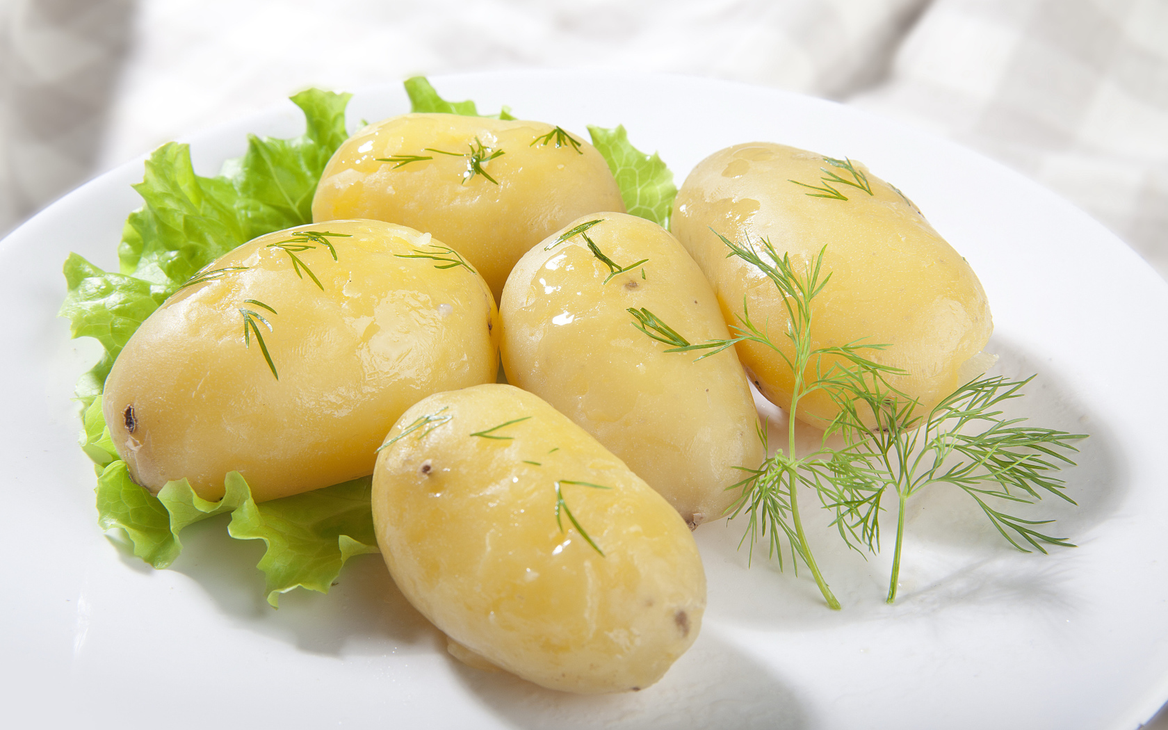 Вареный картофель с листом салата и зеленью на белой тарелке