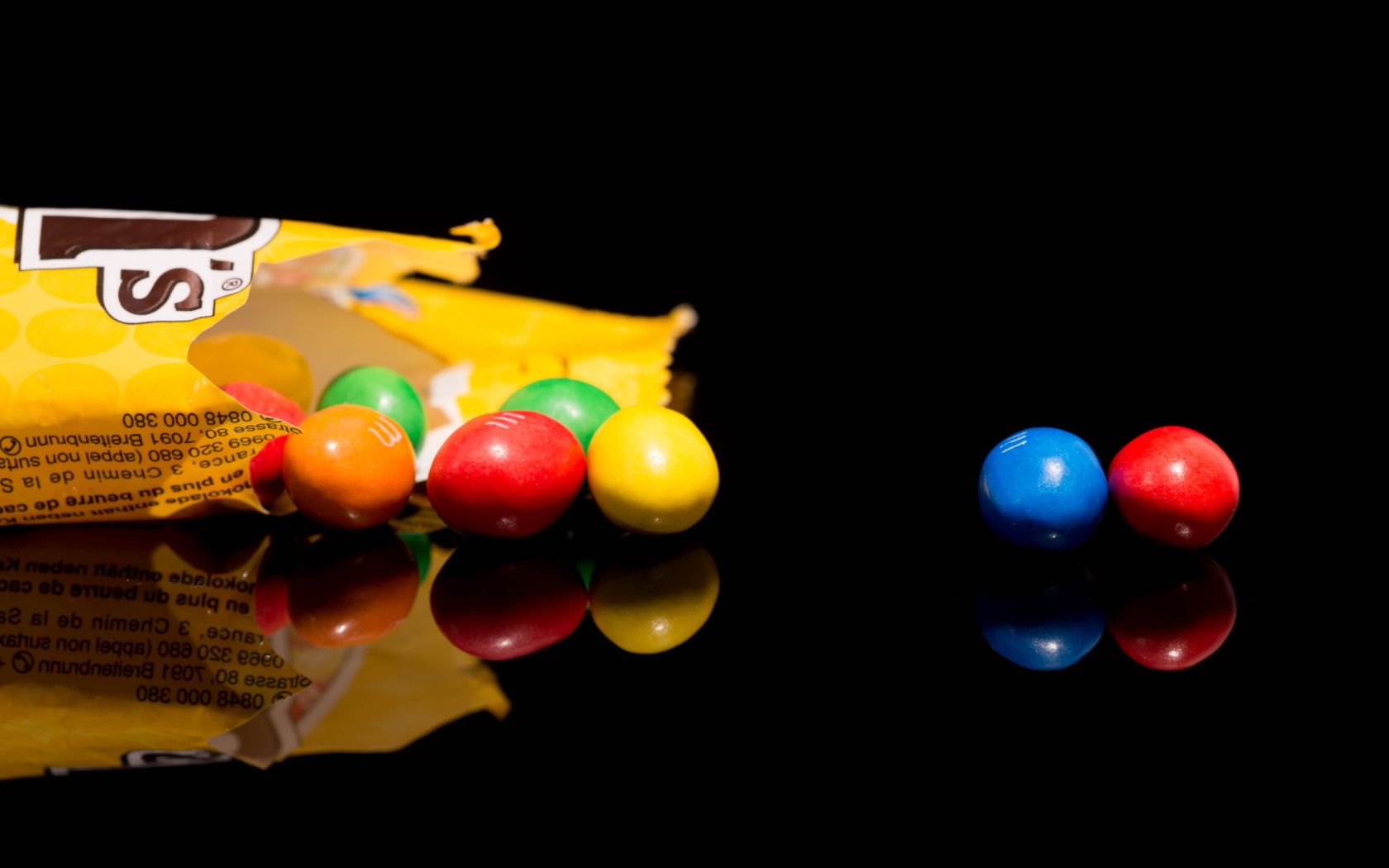 Разноцветные конфеты  M&m's отражаются в черной поверхности стола 