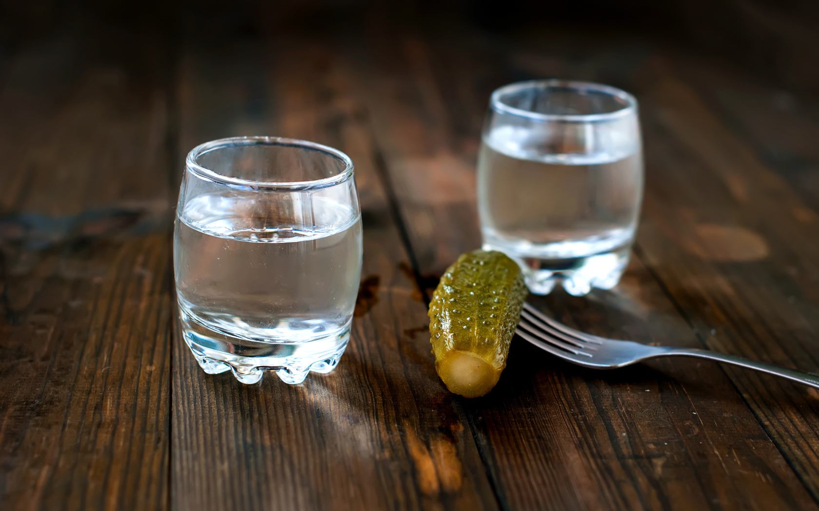 Две рюмки водки и соленый огурец на столе