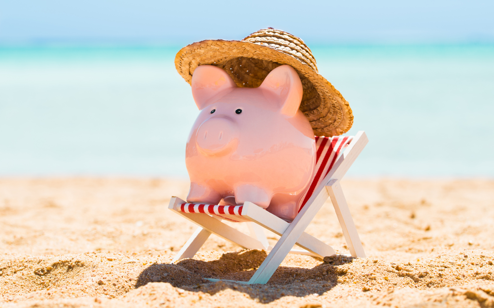 Сувенир свинка в шляпе лежит в игрушечном кресле на пляже