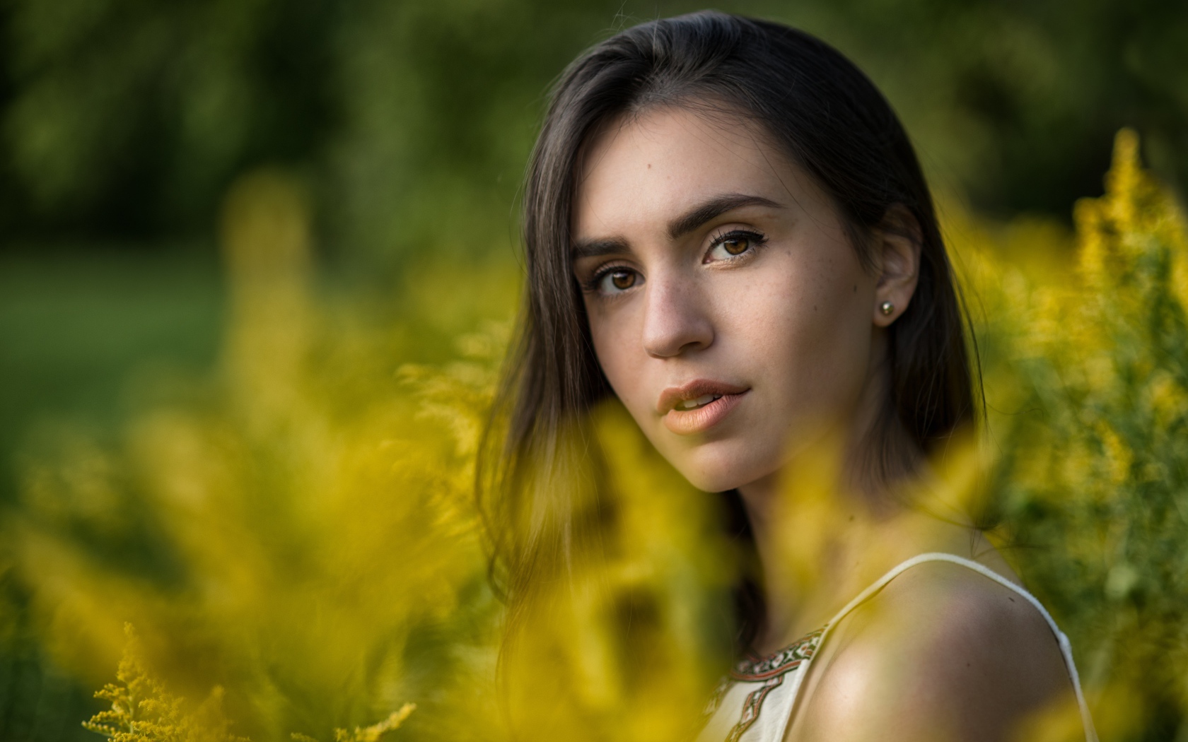 Красивая девушка с нежным взглядом сидит у желтых цветов