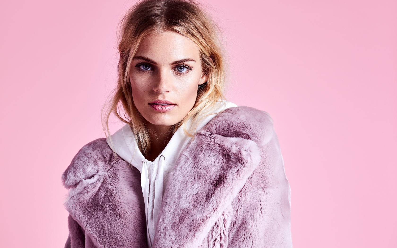 Красивая голубоглазая девушка в шубе на розовом фоне