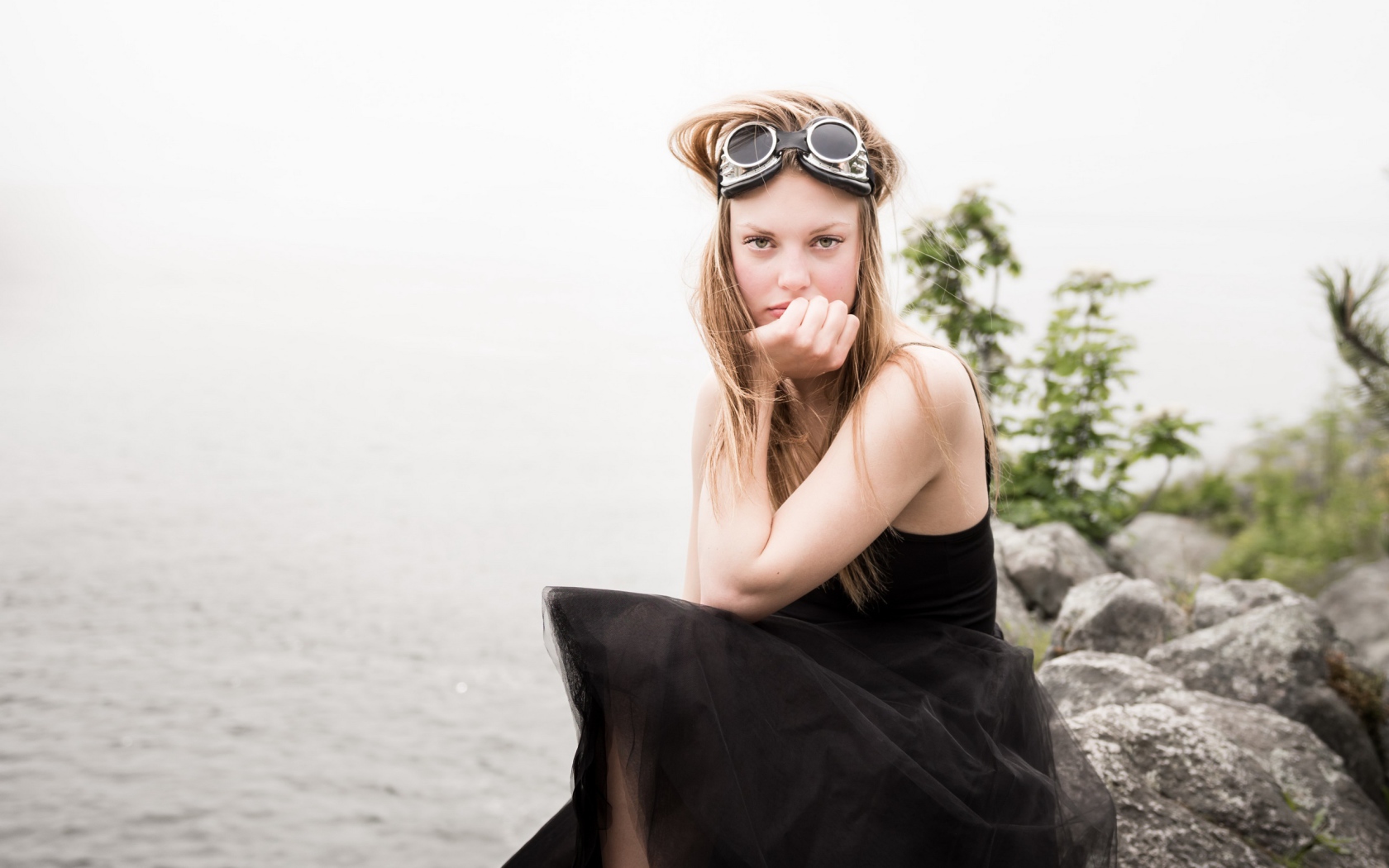 Девушка блондинка с очками на голове сидит на камне