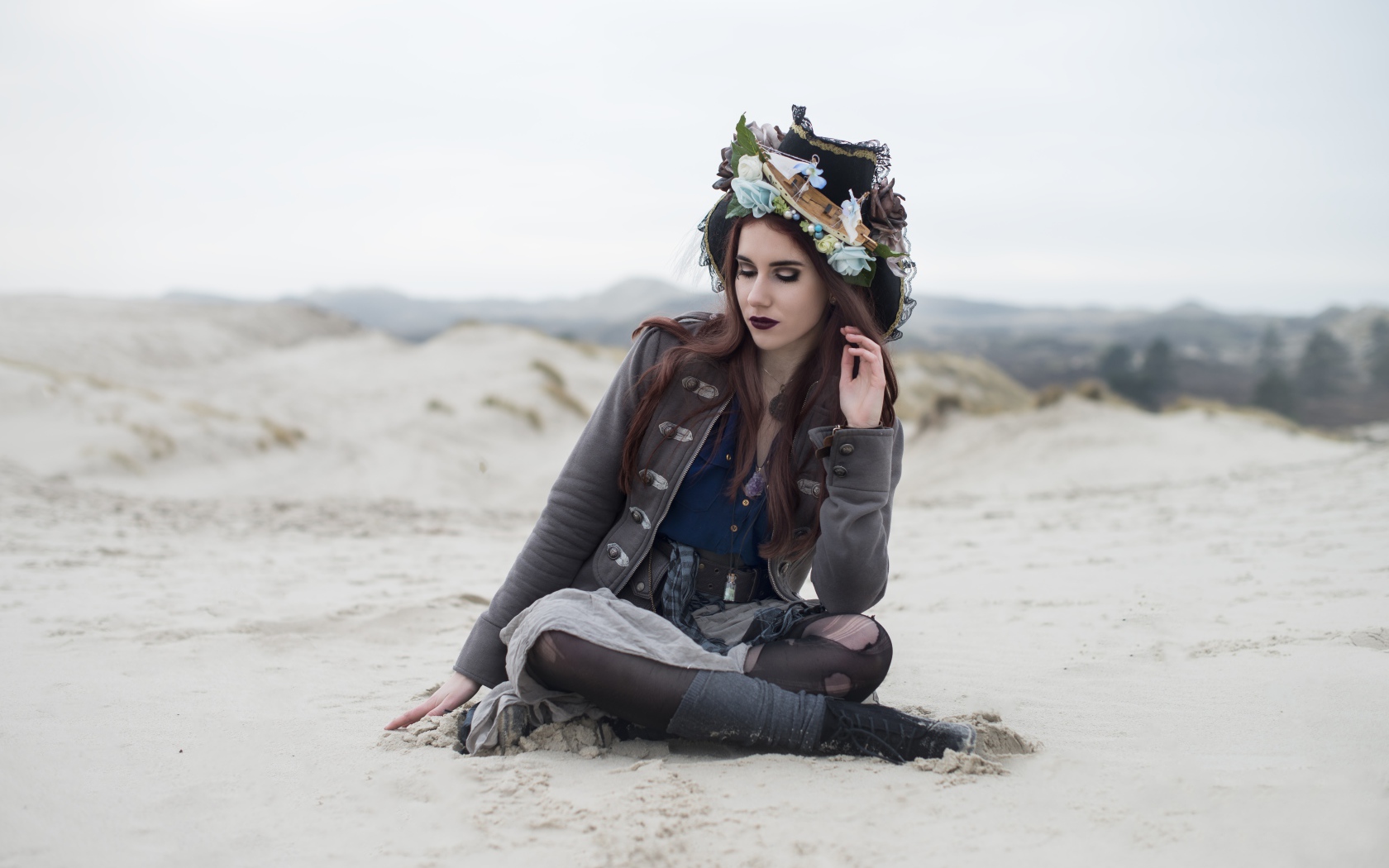 Девушка брюнетка  в костюме сидит на песке 