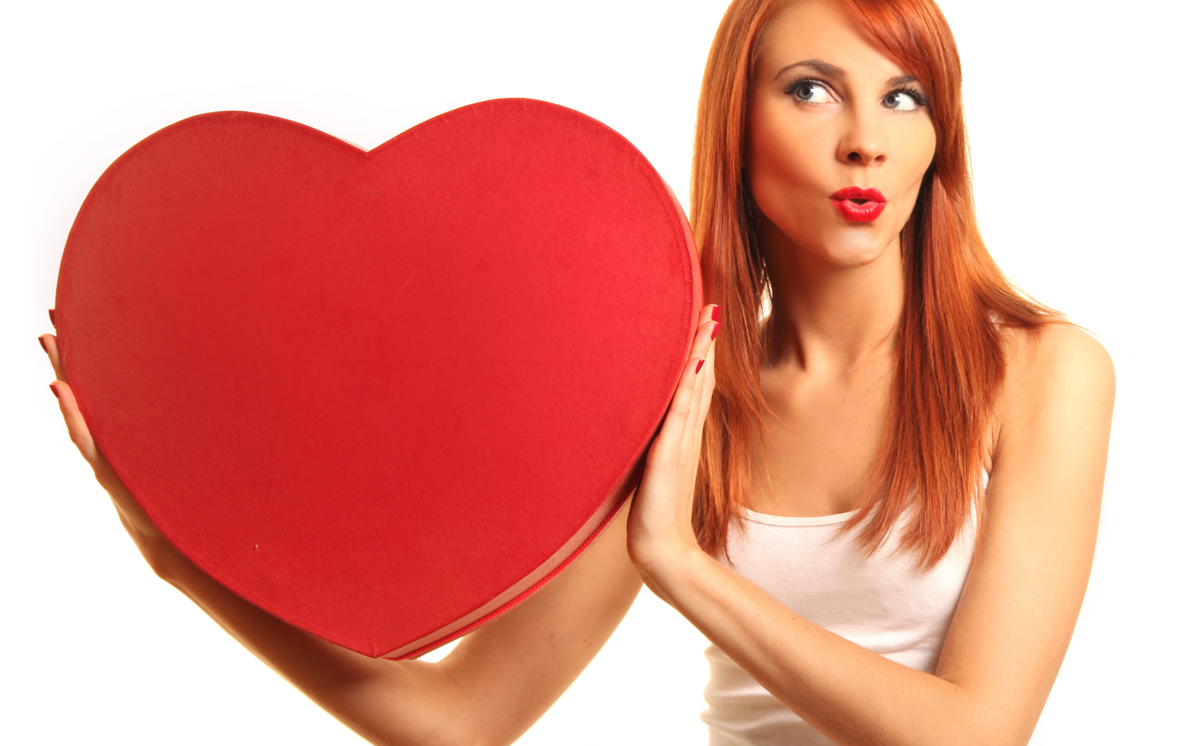 Рыжеволосая девушка с большим красным сердцем в руках на белом фоне