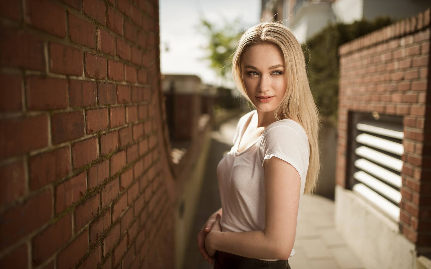 Молодая девушка блондинка у кирпичной стены 