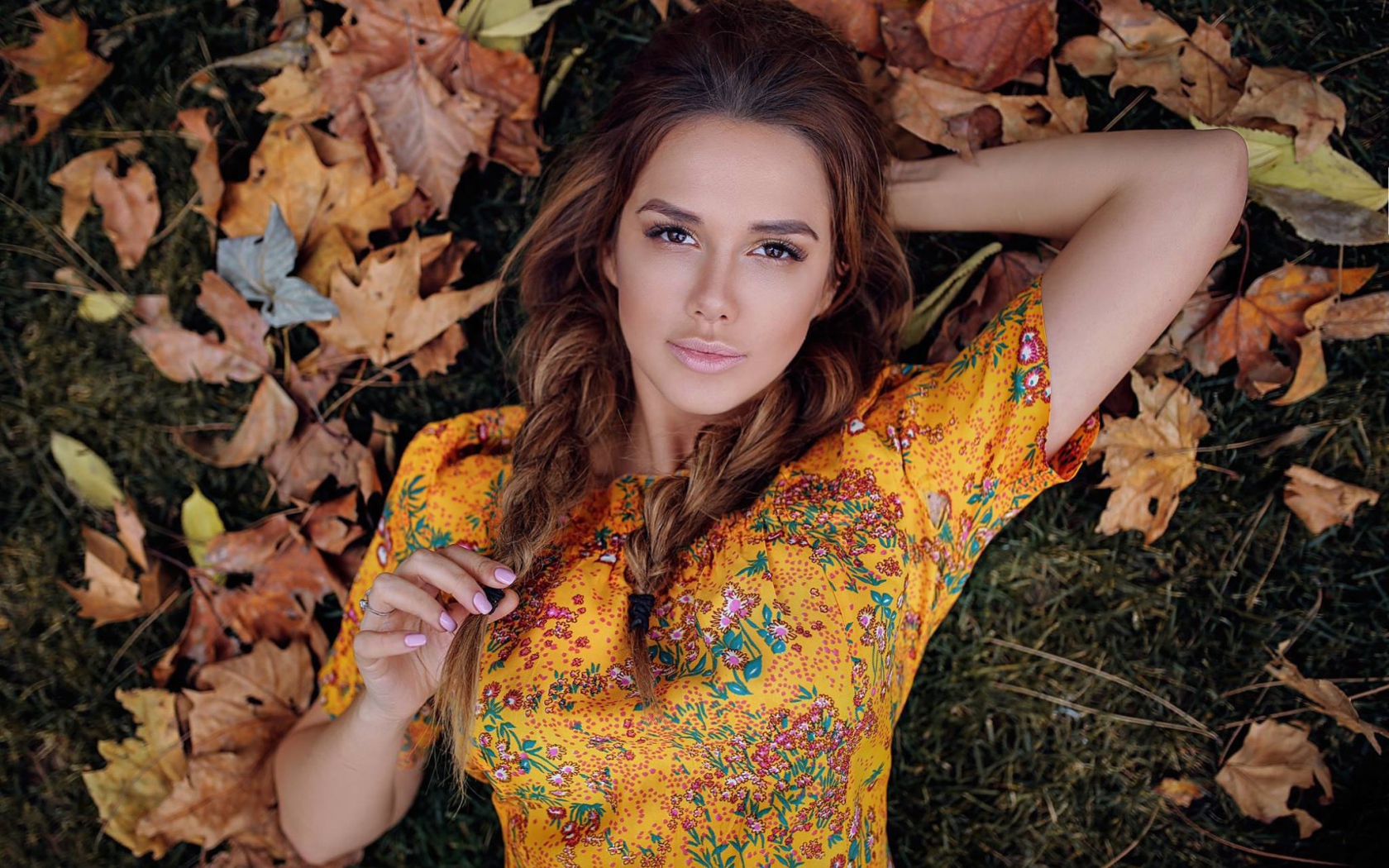 Молодая брюнетка лежит на траве с сухими листьями