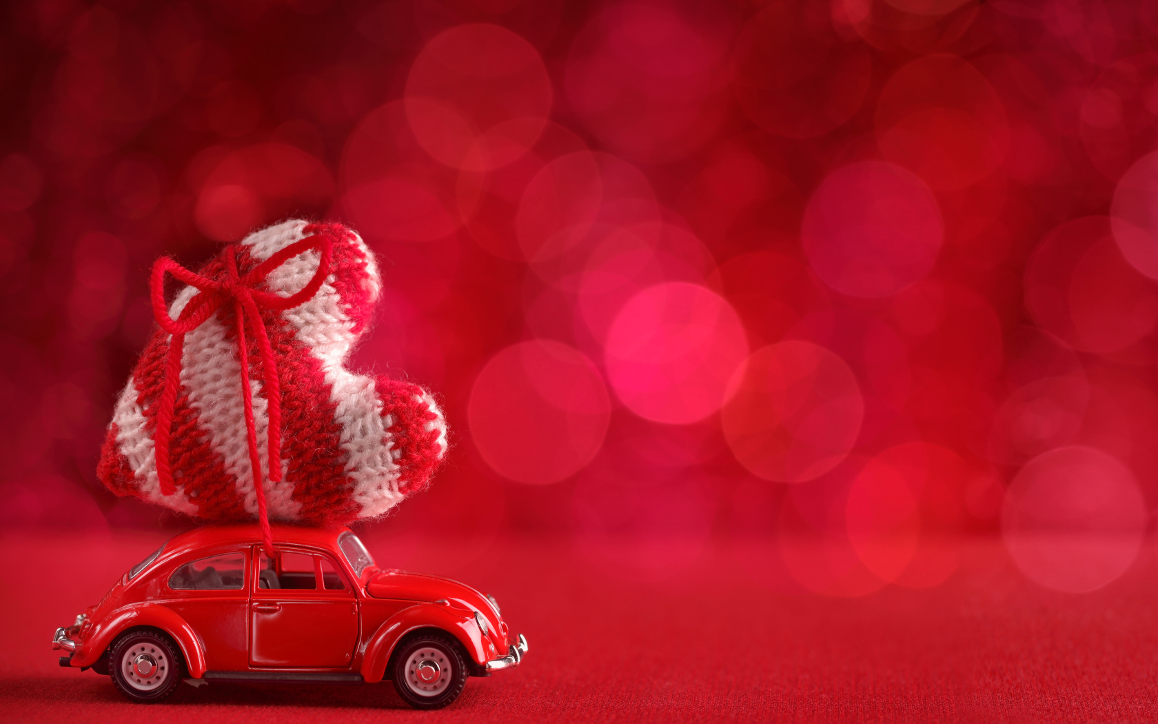 Красная игрушечная машинка везет с сердечко на розовом фоне, фон для открытки на День Святого Валентина
