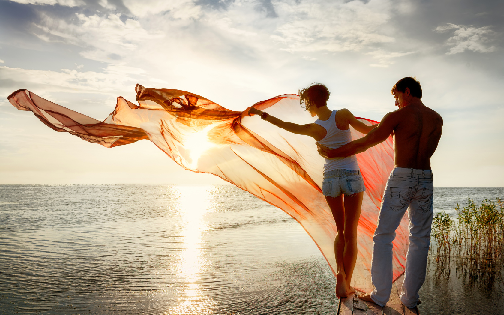 Молодая влюбленная пара гуляет у моря на закате