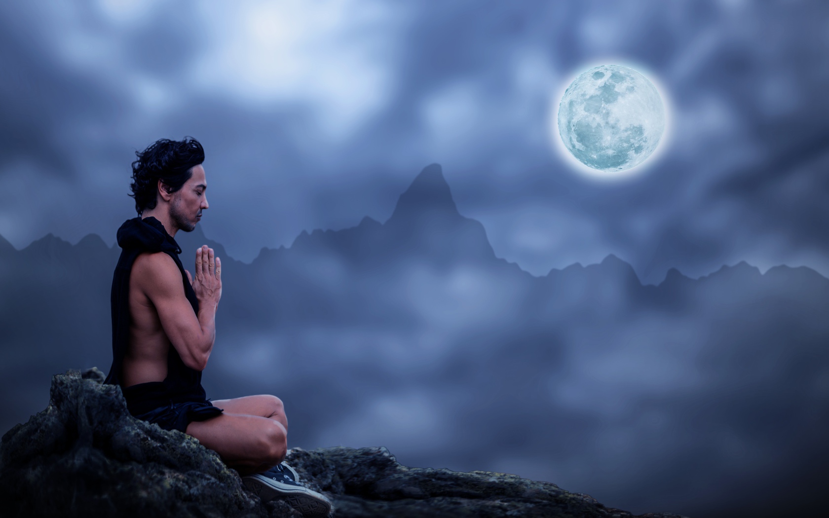 A man meditates on a stone at night on a full moon