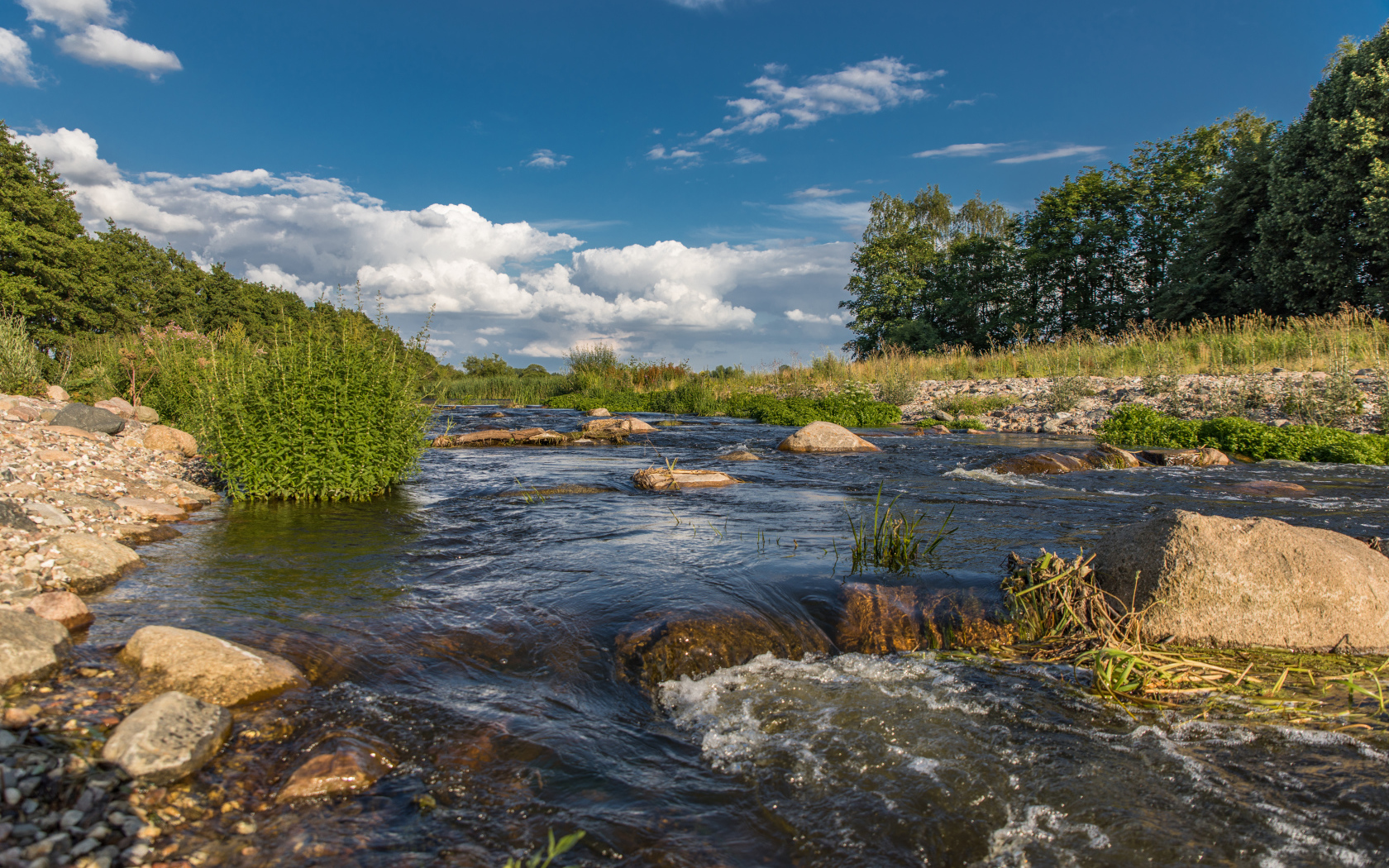 Быстрая речная вода стекает по камням под красивым голубым небом