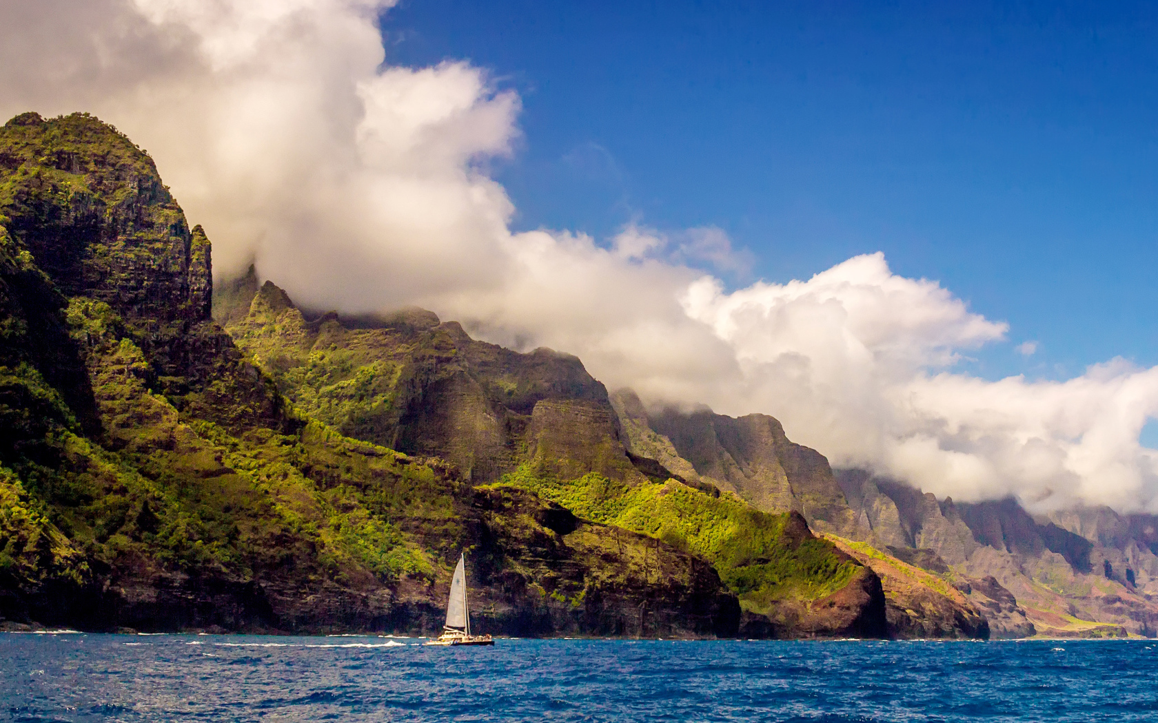 Парусная лодка плывет по голубой воде на фоне покрытых зеленью гор