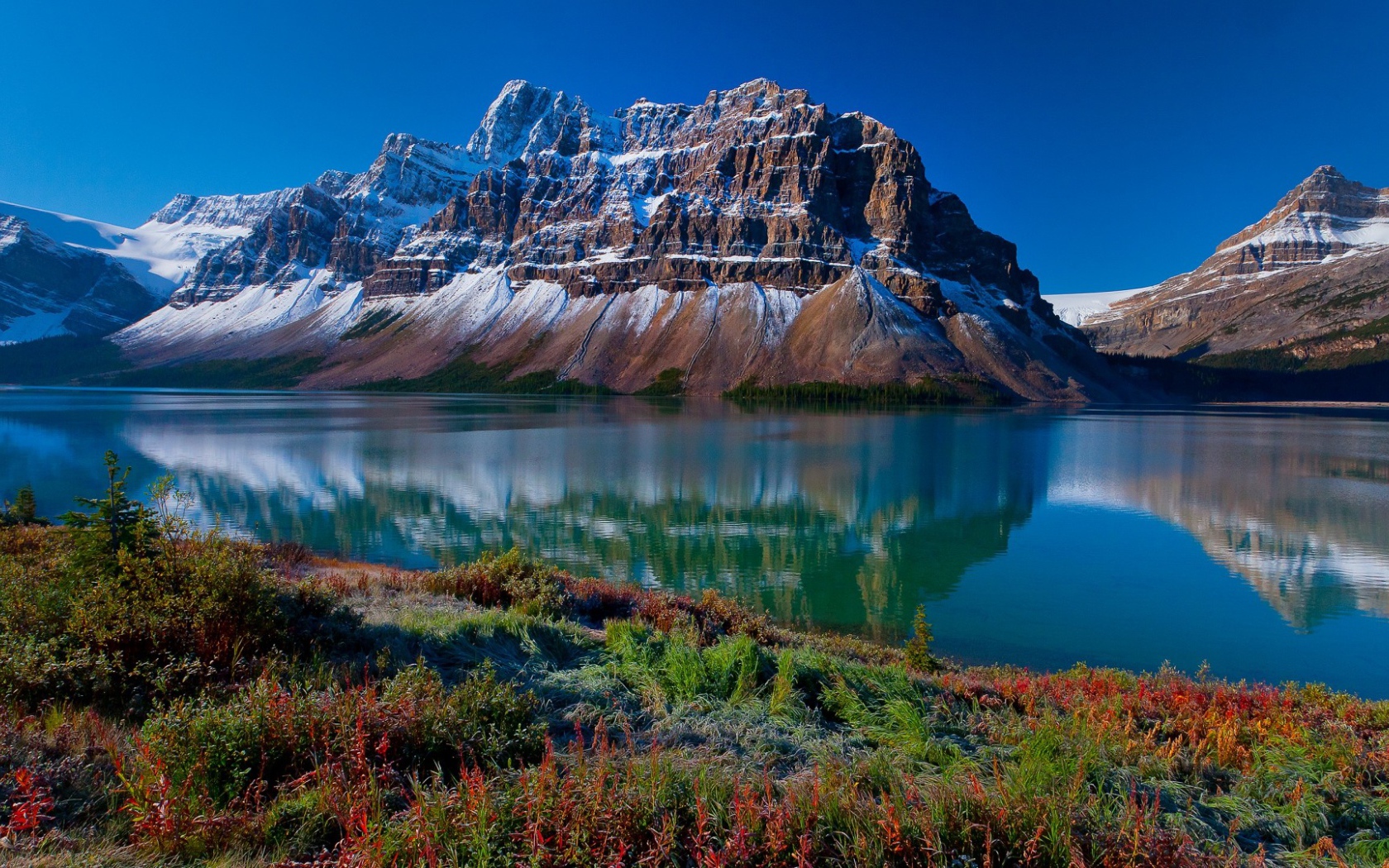 Заснеженные горы отражаются в голубой глади воды 