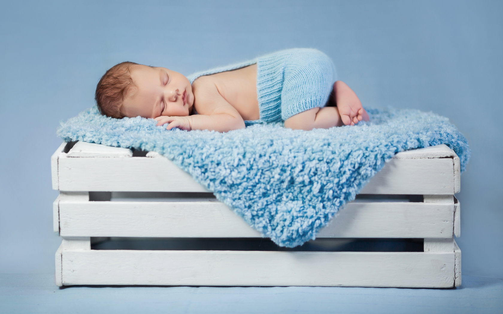 Маленький грудной ребенок спит на синем покрывале на деревянном ящике