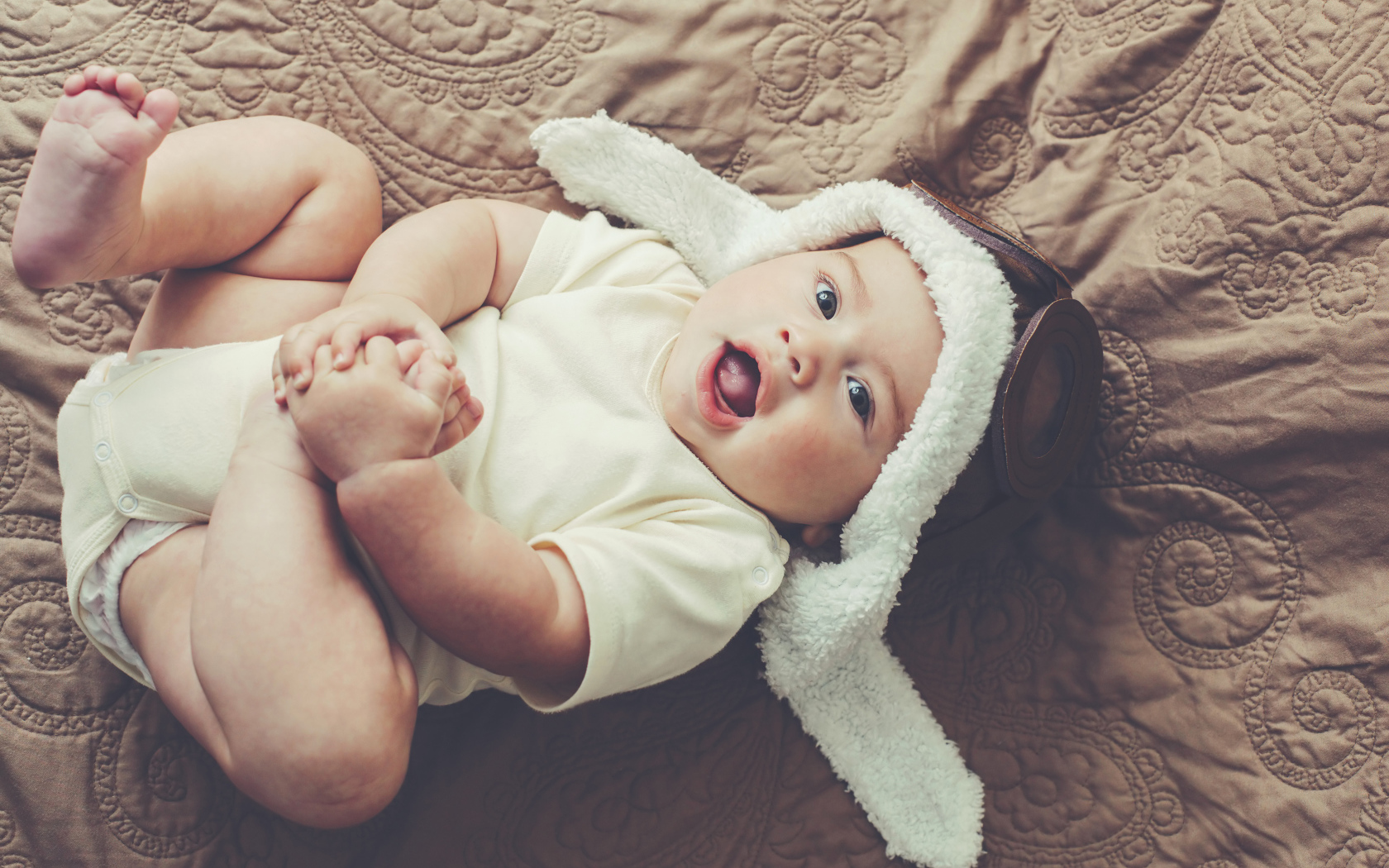 Маленький грудной ребенок лежит в шапке летчика