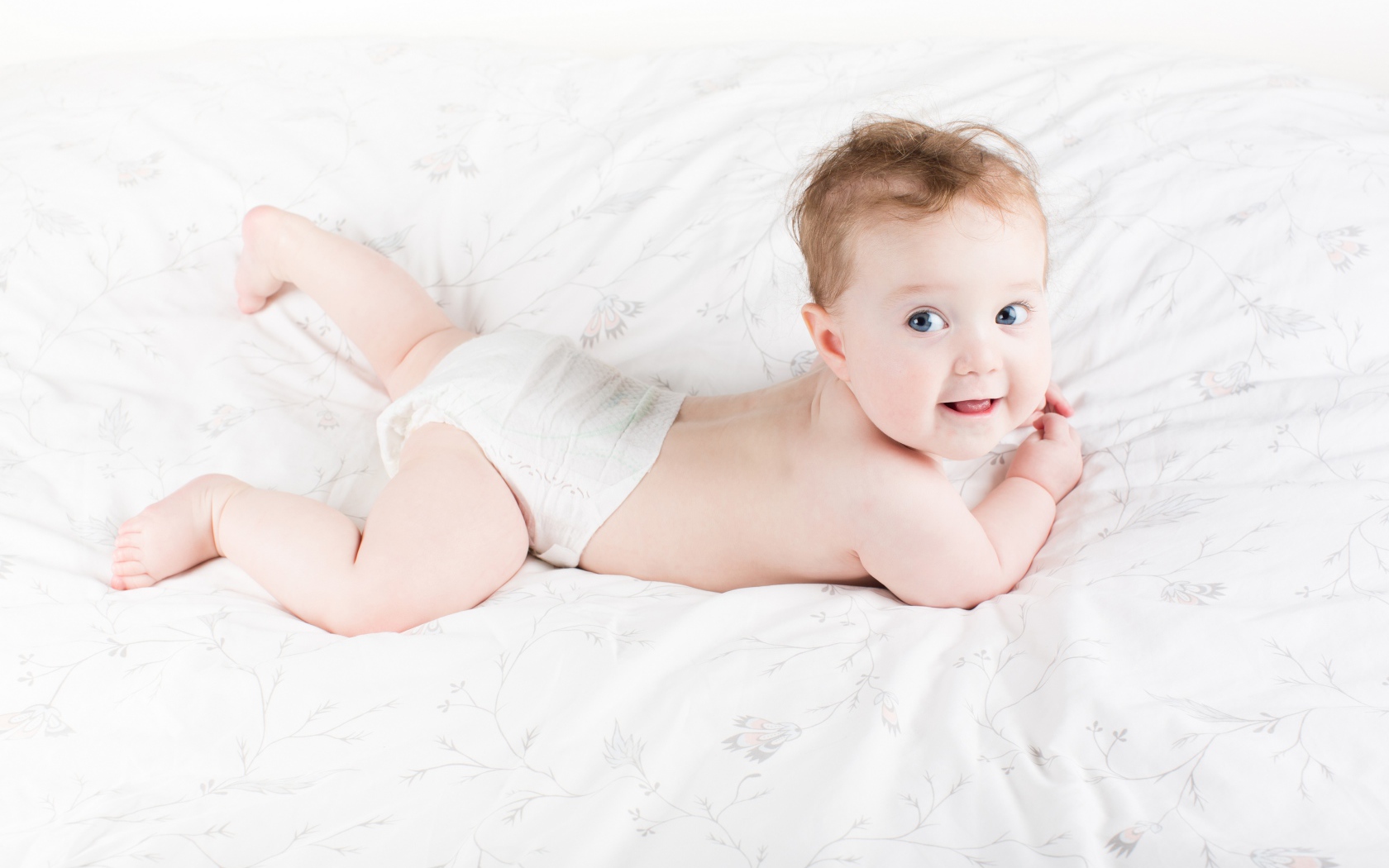 Забавный голубоглазый малыш лежит на белом покрывале