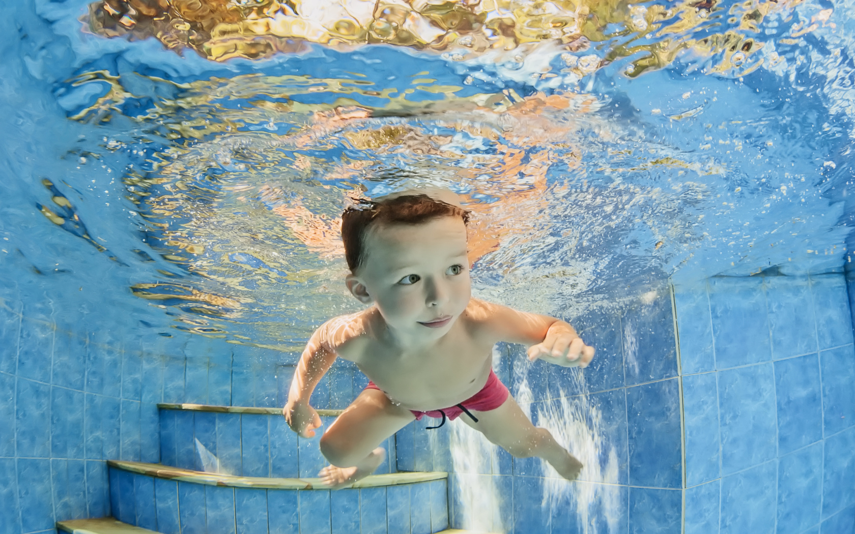Маленький мальчик плавает под водой в бассейне