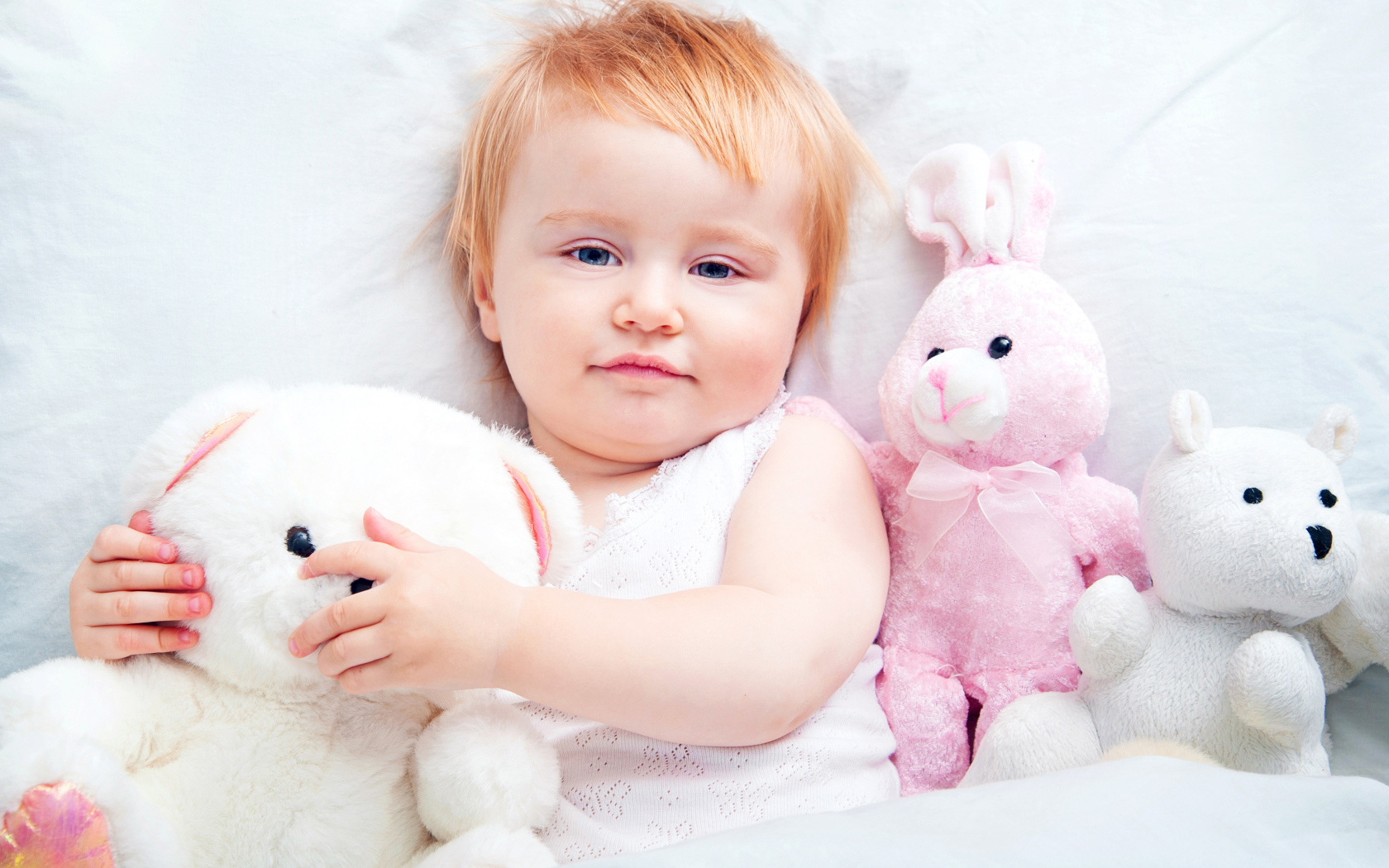 Маленькая девочка лежит в кровати с плюшевыми игрушками