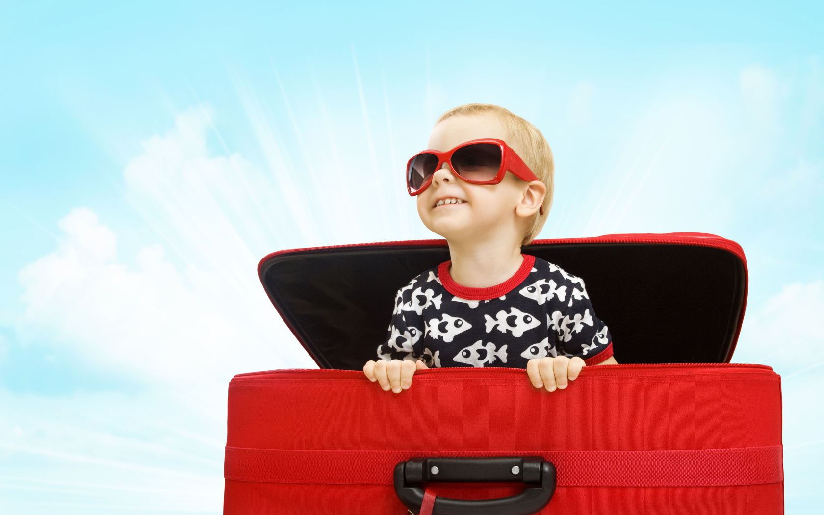 Маленький улыбающийся мальчик в очках сидит в красном чемодане