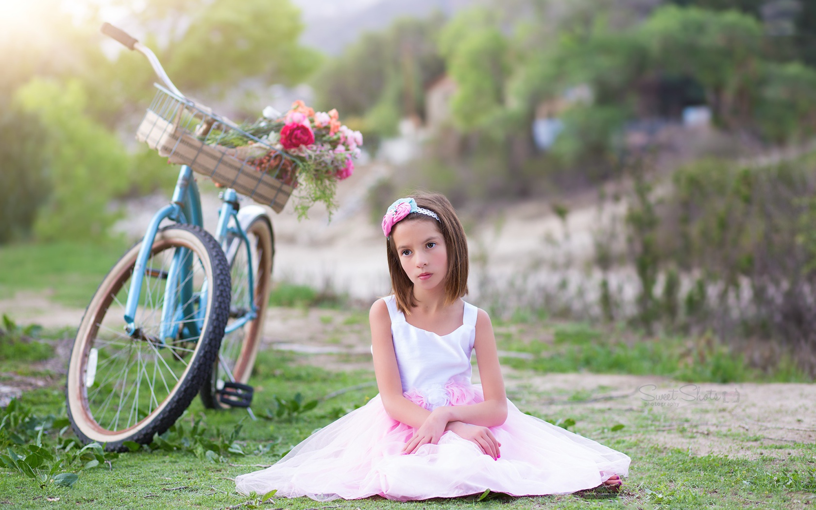 Грустная девочка в красивом платье сидит на траве с велосипедом