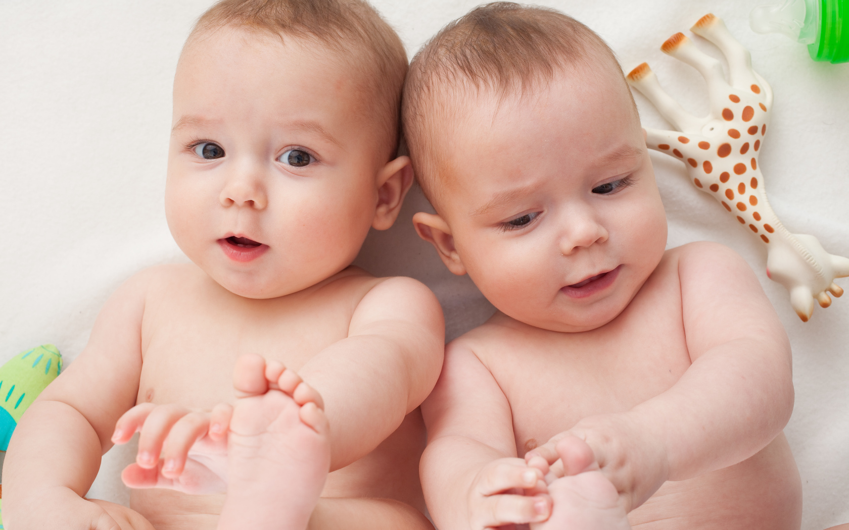 Два маленьких грудных ребенка близнеца с игрушкой